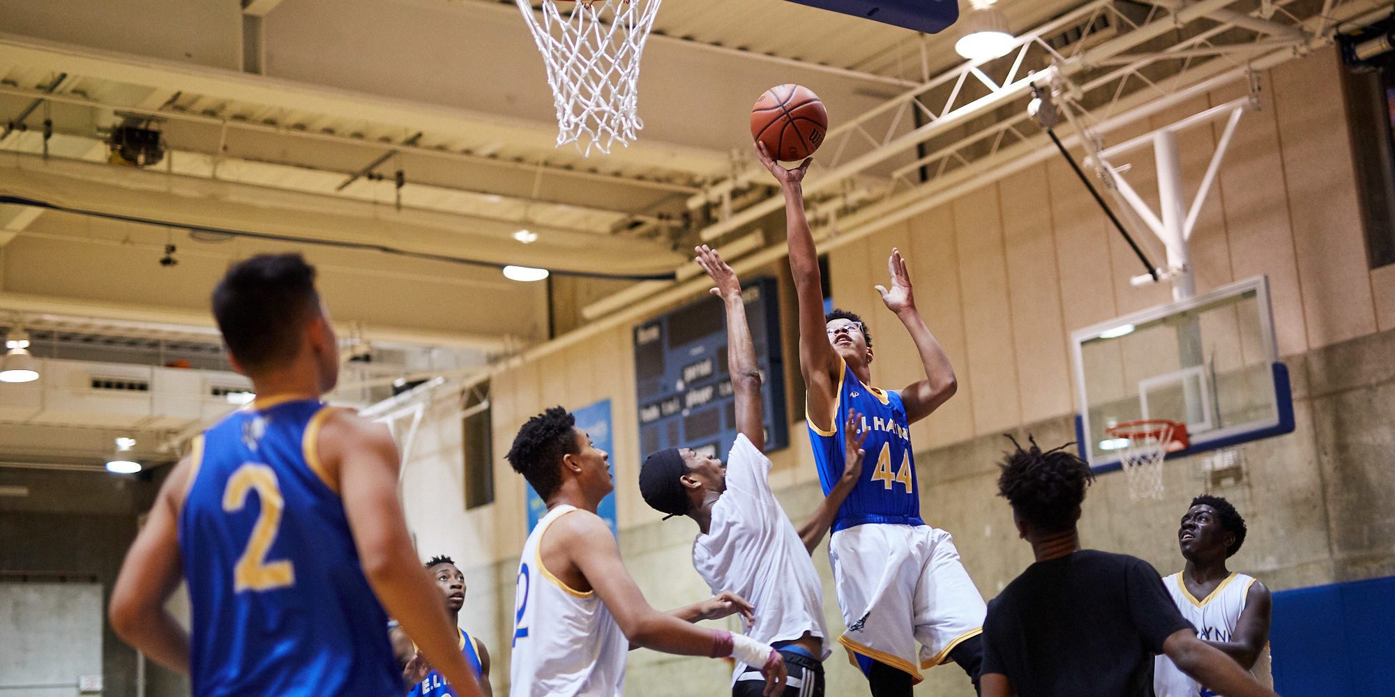 Photograph of a uniformed E.L. Haynes basketball player shooting a basket while surrounded by others.